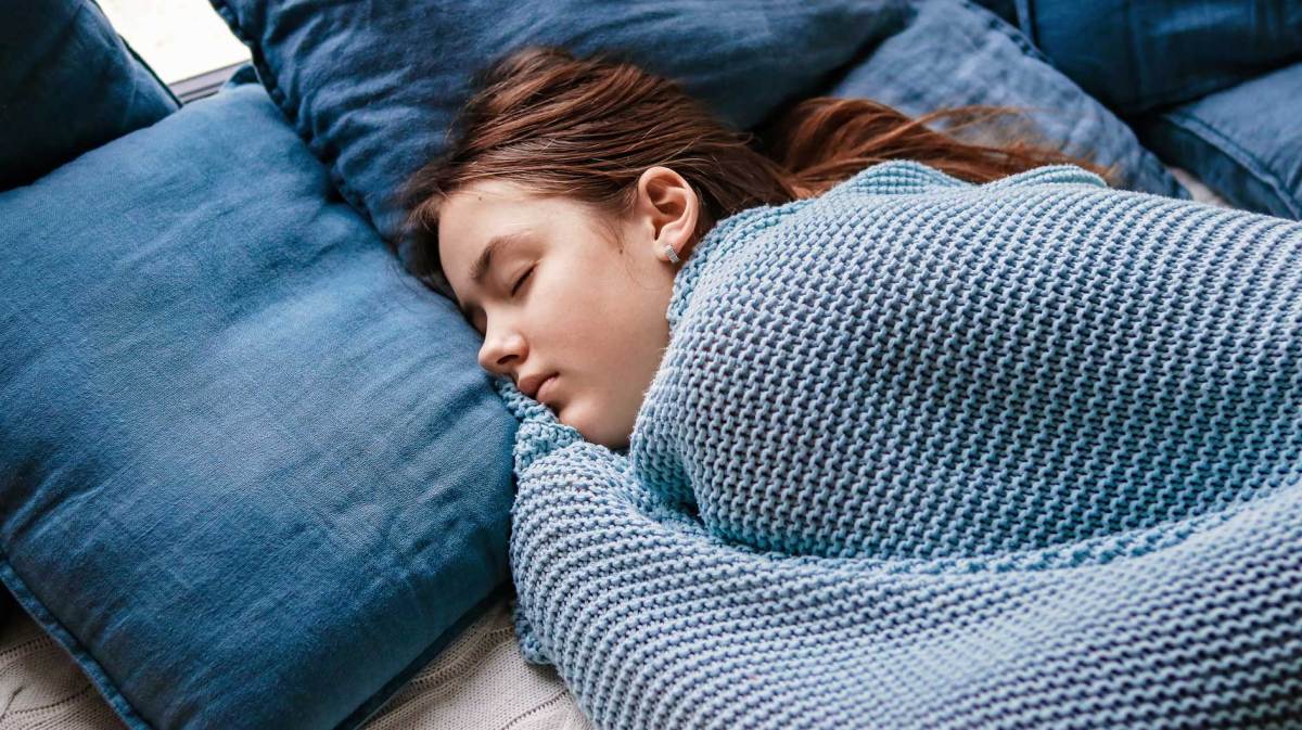 Mädchen im Teenageralter liegt im Bett, zugedeckt mit einer leichten Decke.