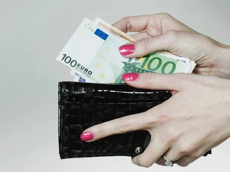 Frau legt Geldscheine in ein dunkles Portemonnaie.