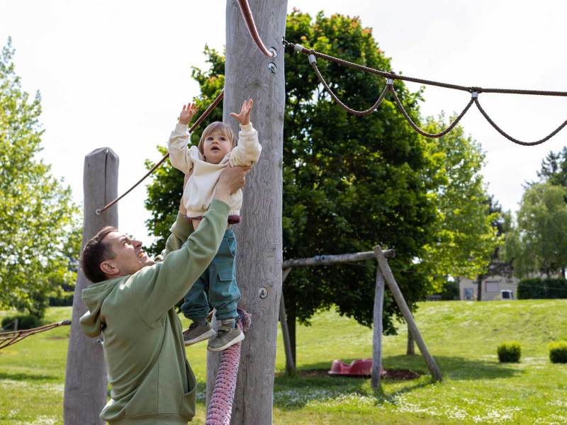 Vater hilft seinem ca. 4-j&auml;hrigen Kind an ein Kletterger&uuml;st.