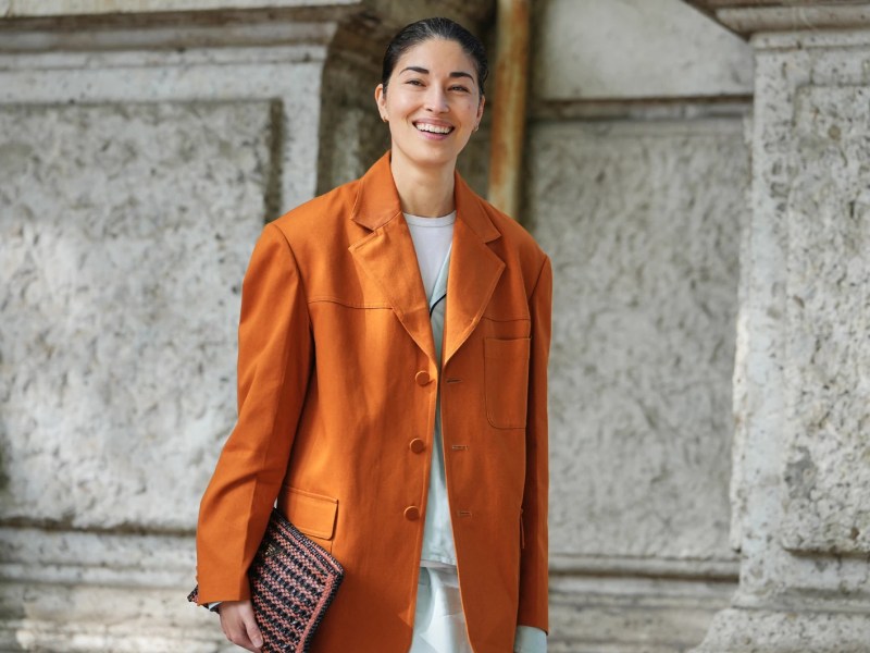Model tr&auml;gt einen orangefarbenen Blazer und hat ihre Haare zu einem Dutt gestylt.