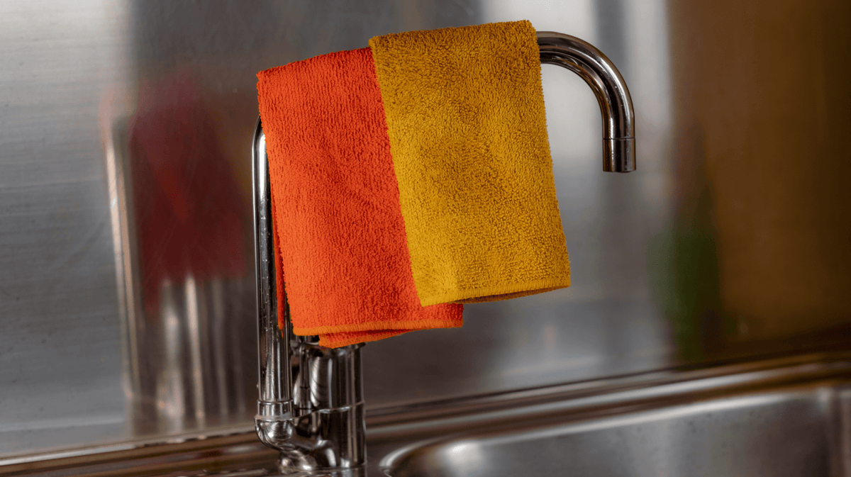 Gelber und Orangener Lappen trocknen auf dem Wasserhahn der Küchenspüle.