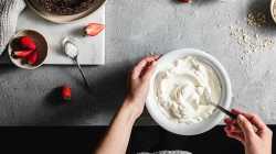Pov-Aufnahme einer K&ouml;chin, die Joghurt in einer Sch&uuml;ssel in der K&uuml;che mit Zutaten auf der K&uuml;chentheke mischt.