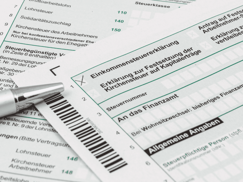 Steuerformulare liegen auf Tisch, ein Kulli daneben.