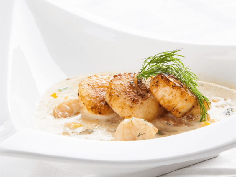 Suppe mit Jakobsmuscheln in einer weißen Schüssel.
