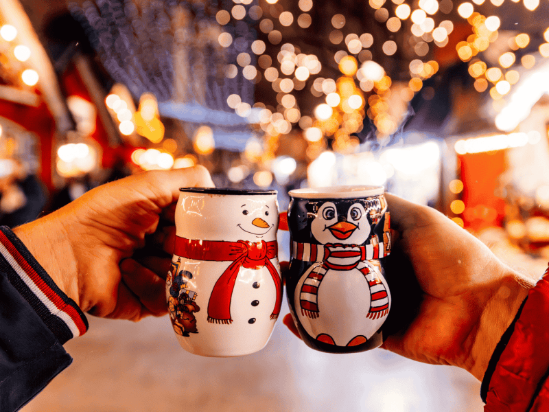 Personen stoßen mit weihnachten Tassen auf Weihnachtsmarkt an.