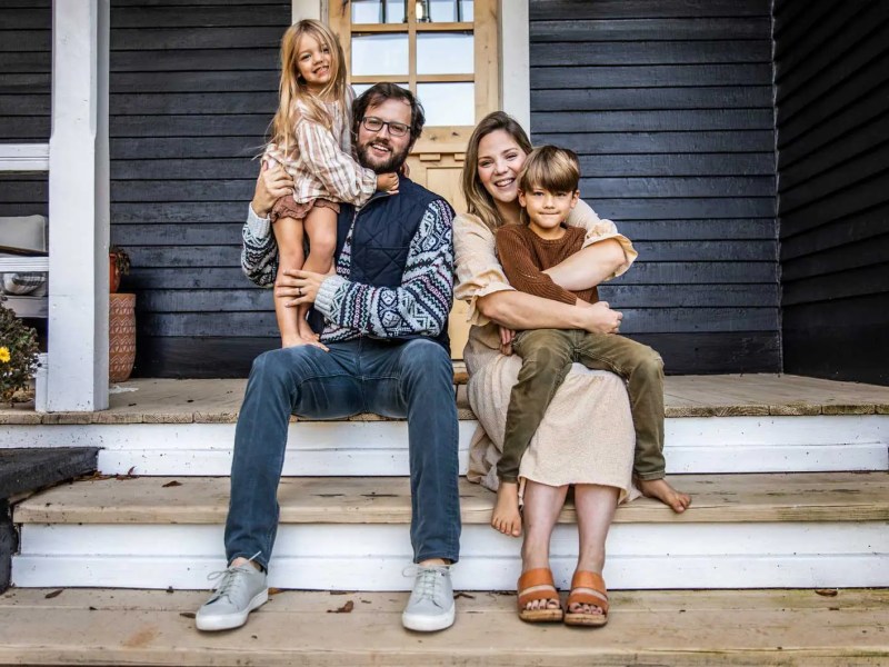 Mutter, Vater und zwei Kinder sitzen auf der Veranda ihres Hauses und posieren für ein Familienfoto.