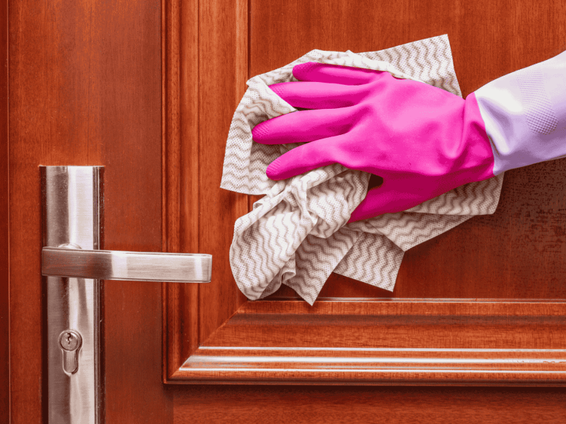 Person mit pinkem Putzhandschuhe wischt mit Lappen über Wohnungstür.