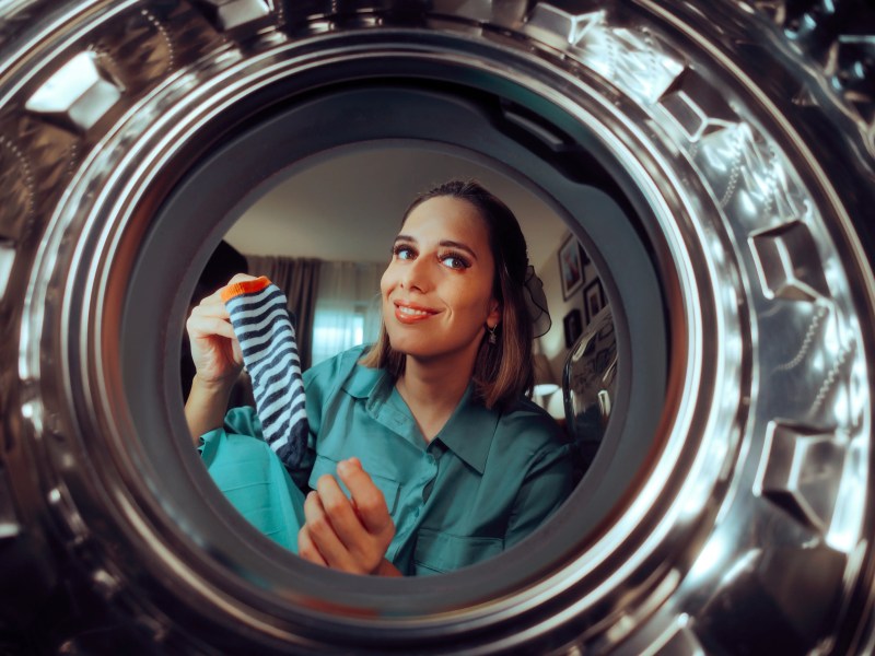 Frau guckt in eine leere Waschmaschine und h&auml;lt eine Socke in der Hand