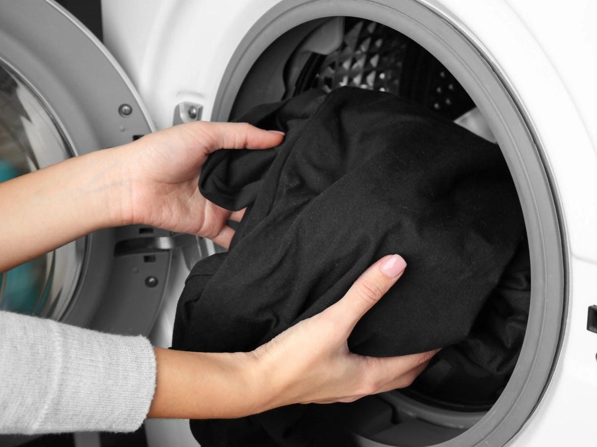Nahaufnahme von Frauenh&auml;nden, die schwarze W&auml;sche in die Waschmaschine packen