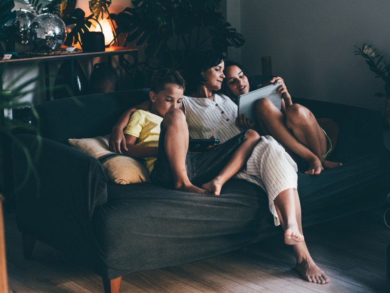 Mutter mit ihren beiden Kindern abends auf dem Sofa.
