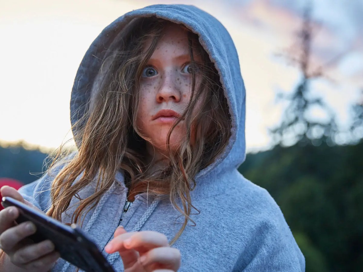 Mädchen im Hoodie am Telefon schaut erschrocken in die Kamera.