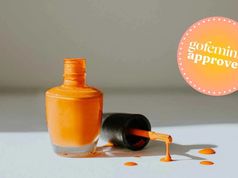Nagellack in Orange. Der Pinsel liegt daneben mit einigen Tropfen Nagellack.