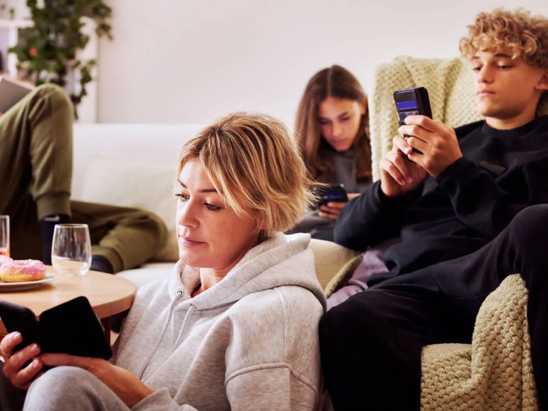Familie zu Hause im Wohnzimmer, aber jeder ist an seinem Handy und mit sich besch&auml;ftigt.