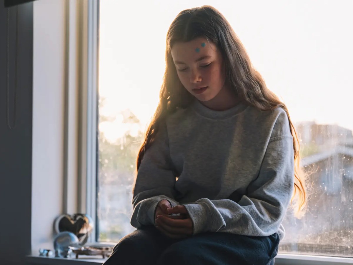 Teenagerm&auml;dchen sitzt auf der Fensterbank und schaut auf ihr Handy.